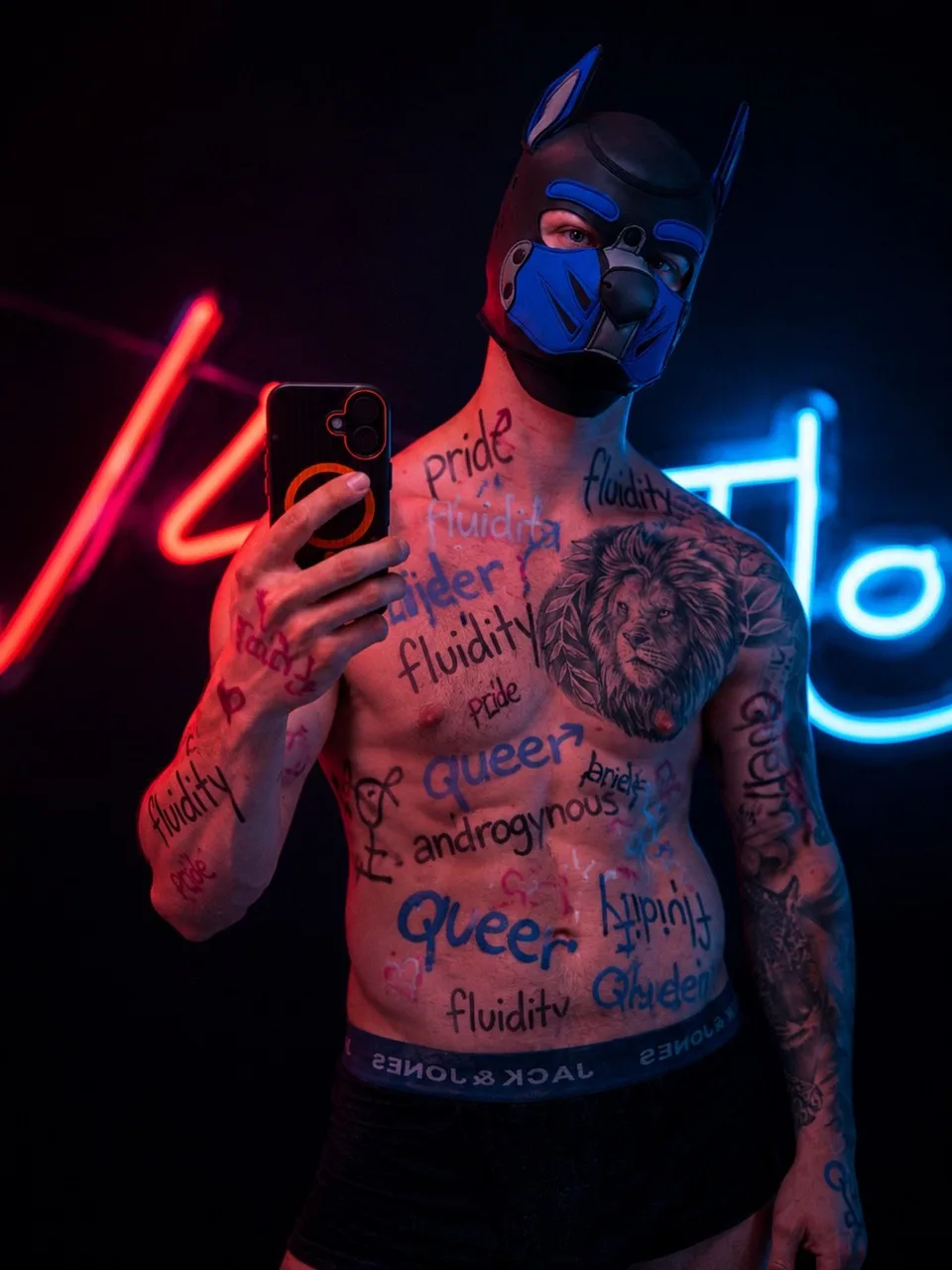 Pup Bacu in a neon-lit room, phone in hand, pride words written on his skin.